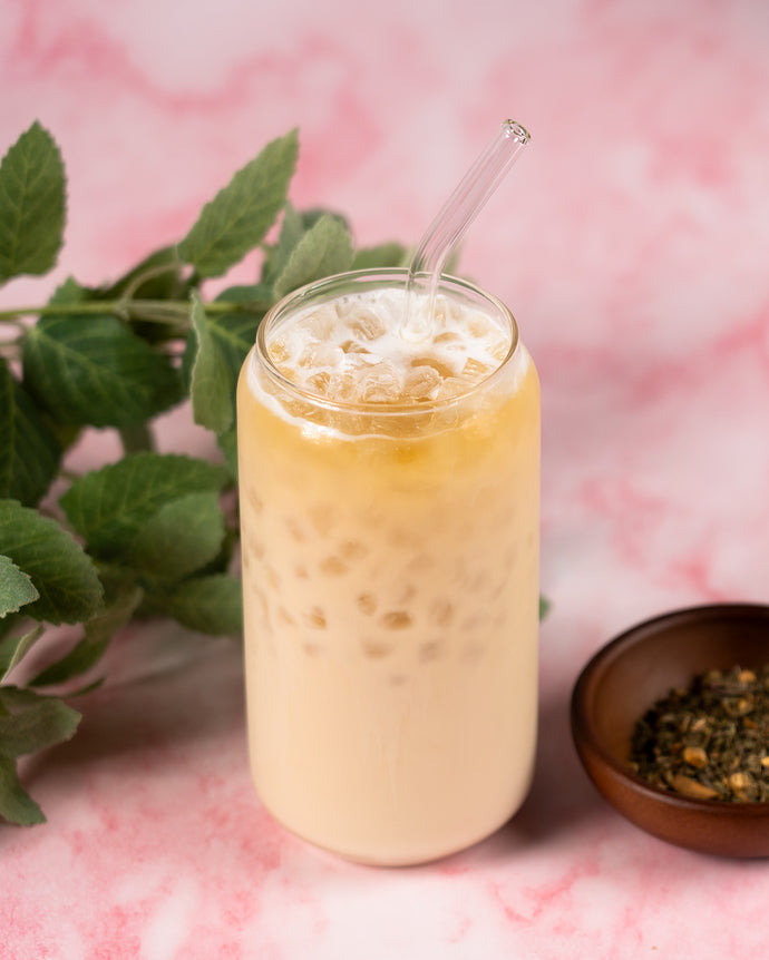 Glass of creamy beverage with a straw on a pink marble surface with green leaves and a small bowl.