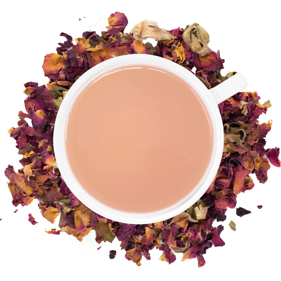 A white mug filled with rose petal tea with rose petals around it. 