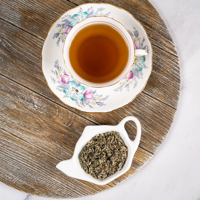 Tea cup with floral design on a wooden surface, accompanied by a small dish of sage leaves.