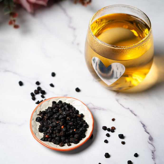 Glass of schisa tea with a heart-shaped sticker, surrounded by berries.