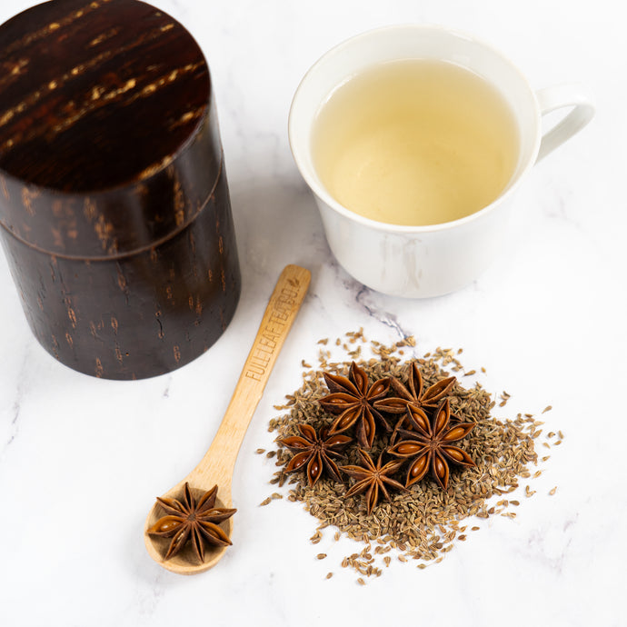 Tea cup with star anise and a wooden container on a white surface