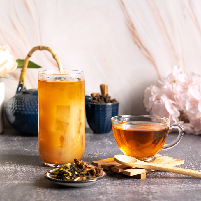 Glass of iced tea and cup of black tea on a table with tea leaves and a spoon.