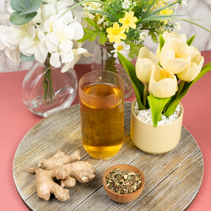 Glass of thyroid tea with ginger root, thyroid tea blend, and a potted plant on a wooden surface.