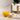 A glass cup of turmeric tea beside a small white bowl and wooden spoon filled with turmeric powder, with a potted plant in the background on a light marble surface.