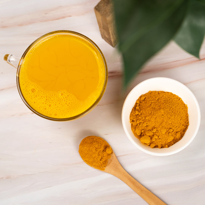 Turmeric tea in a clear mug next to a cup filled with turmeric on a wooden table. 