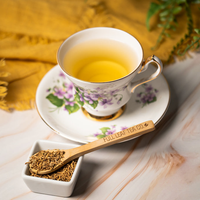 Tea cup with floral design, wooden spoon, and valerian root on a wooden surface.