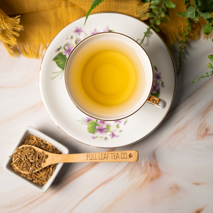 Tea cup with saucer on a marble surface, accompanied by a wooden spoon and valerian root