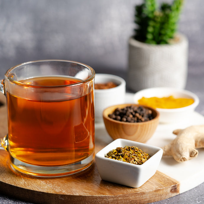 Glass of vertigo relief tea on a wooden board with bowls of spices and a plant in the background