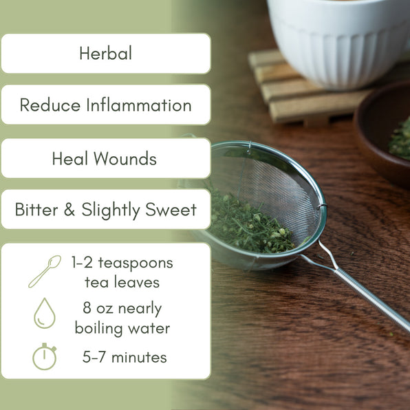 Tea-making setup with a strainer, yarrow leaves, and a cup on a wooden surface.