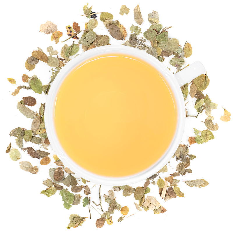 A white mug filled with Bilberry leaf tea surrounded by bilberry leaves