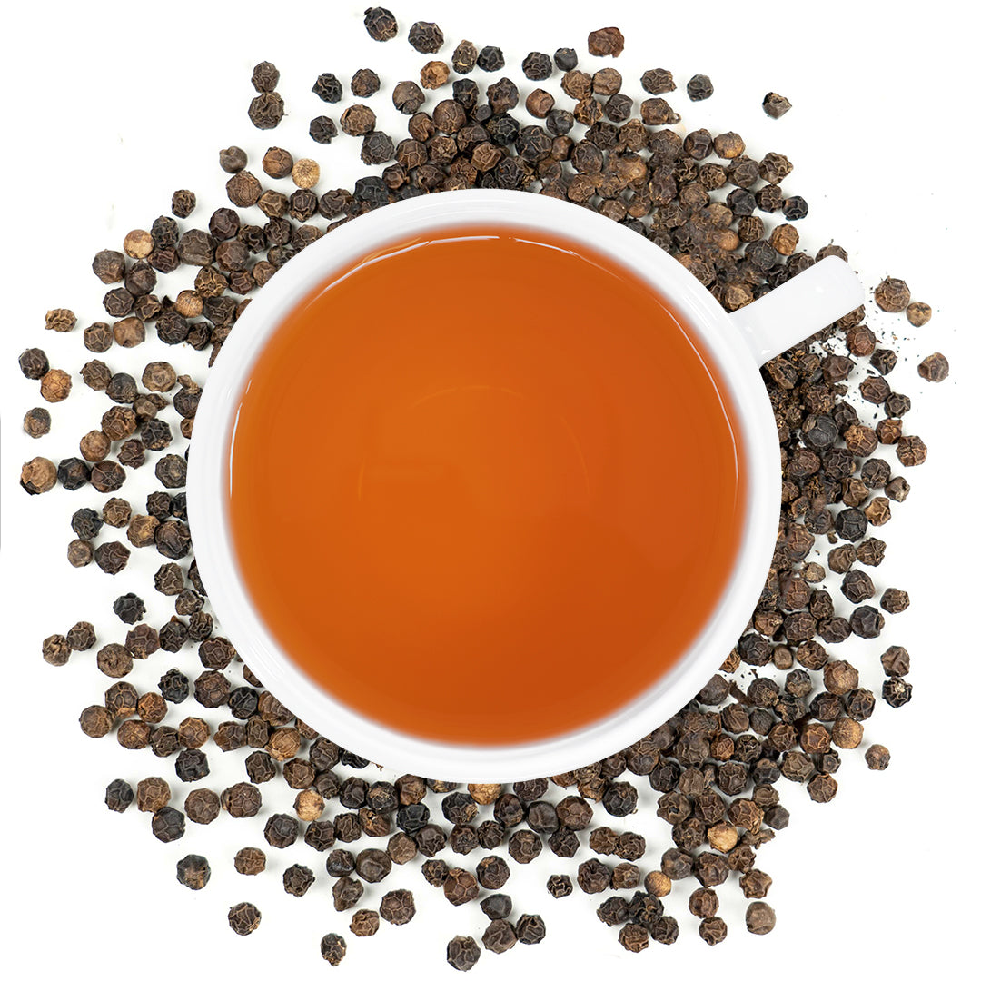 A white mug filled with black pepper tea surrounded by black pepper