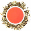 A cup of Organic Blood Pressure Tea with a bright red brew, surrounded by dried herbs and spices used in the tea blend.