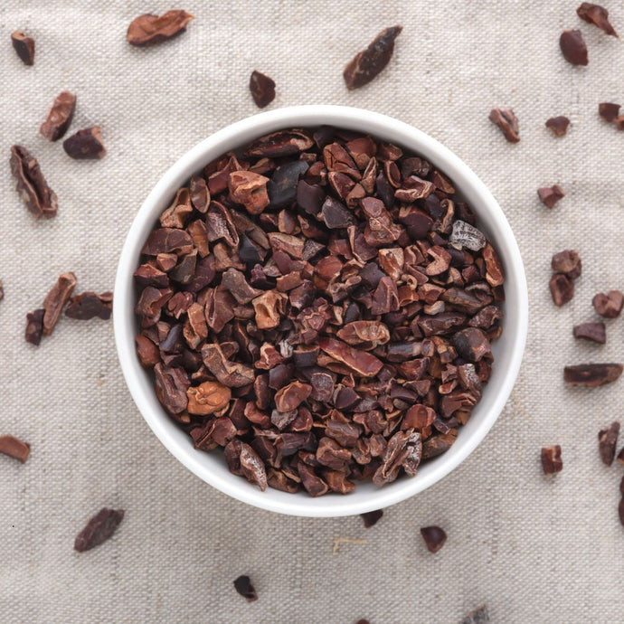 Cacao nibs in a white bowl on a light fabric background