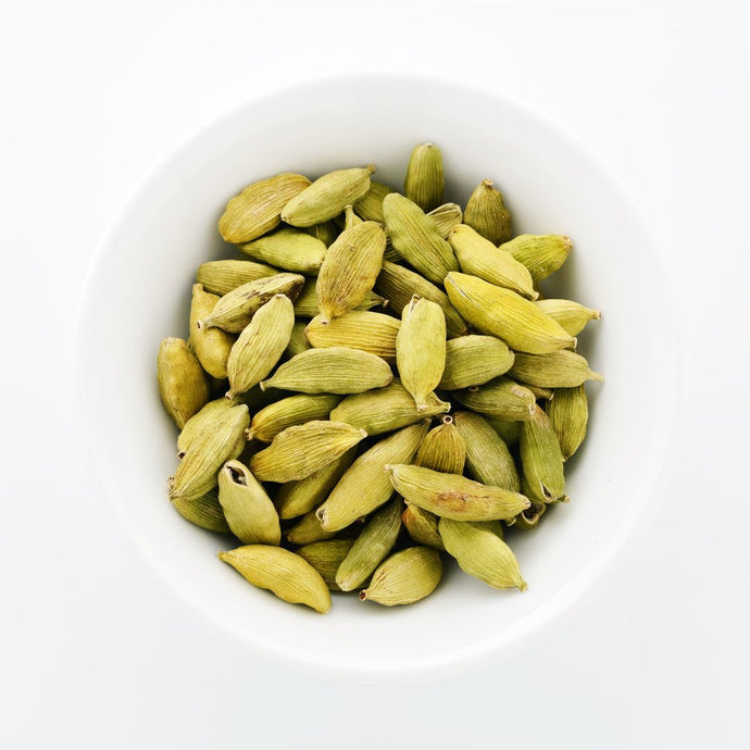 Green cardamom pods in a white bowl on a white background
