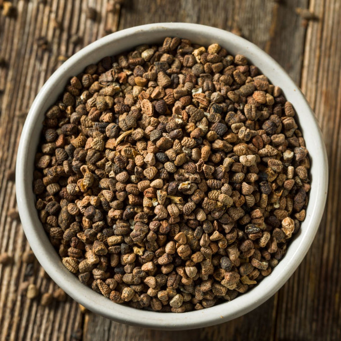 White bowl filled with dried cardamon seeds on a wooden surface