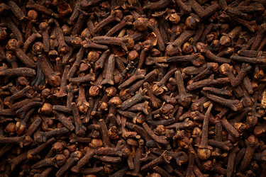Close-up of dried clove buds with a rich brown color and textured surface, showing their distinctive bulbous heads and stems.