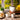 Cozy tea scene with a white teapot, two cups of brewed herbal tea, and wooden bowls of loose leaves on a rustic table near a window with bright green foliage outside.