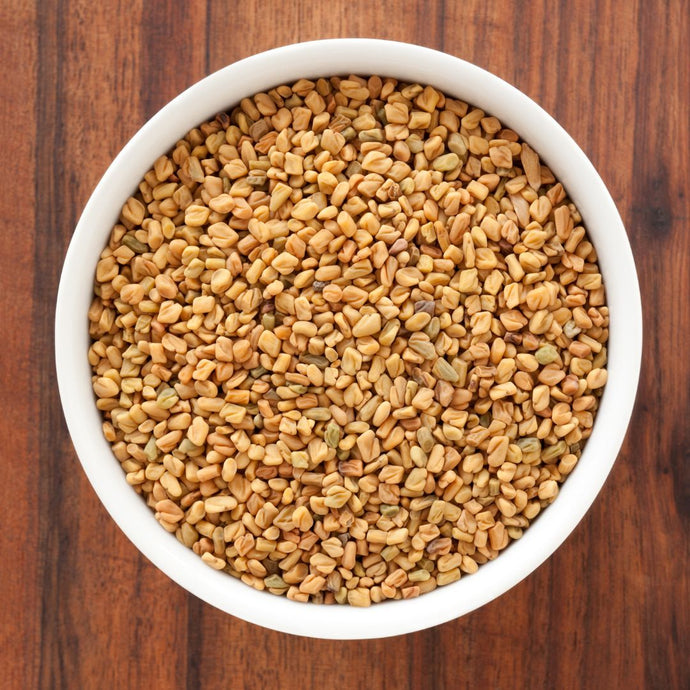 White bowl filled with fenugreek seeds on a wooden surface