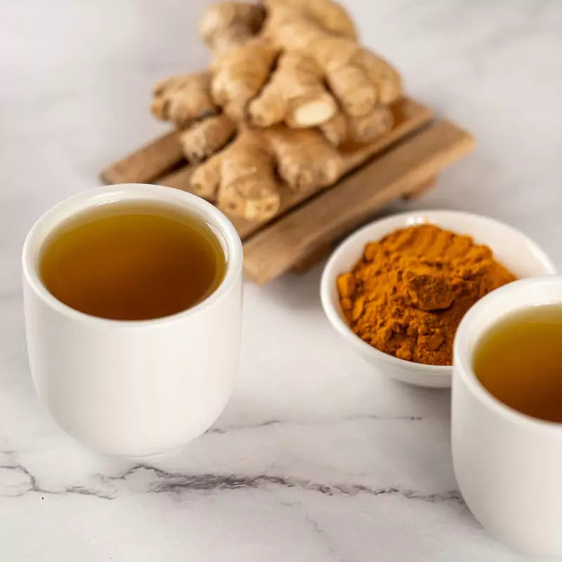 Cup of tea sitting on marble counter, next to ginger root and turmeric