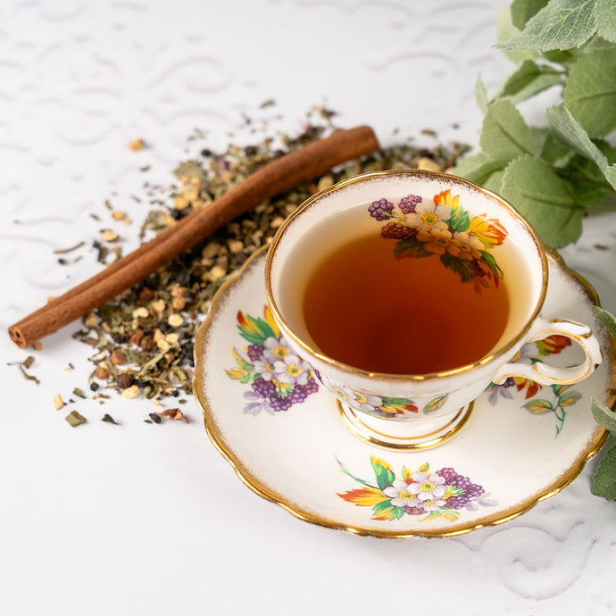 Teacup with floral design filled with tea, cinnamon stick, and herbs on a light background