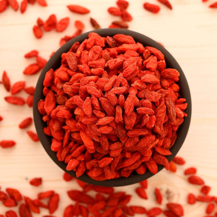 Black bowl filled with red goji berries on a light background