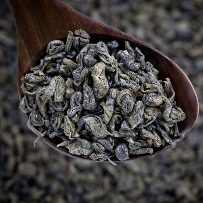 Wooden spoon filled with dried gunpowder green tea leaves against a blurred background
