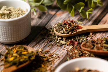 Loose leaf herbal tea blend with wooden spoons and bowls on a rustic wooden surface, featuring dried herbs and botanicals for Full Leaf Tea Co.