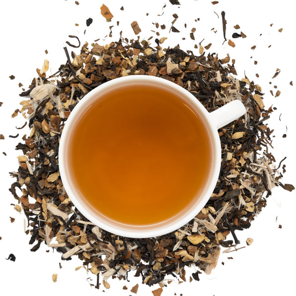White cup of prebiotic tea surrounded by dry prebiotic tea herbs on a white background