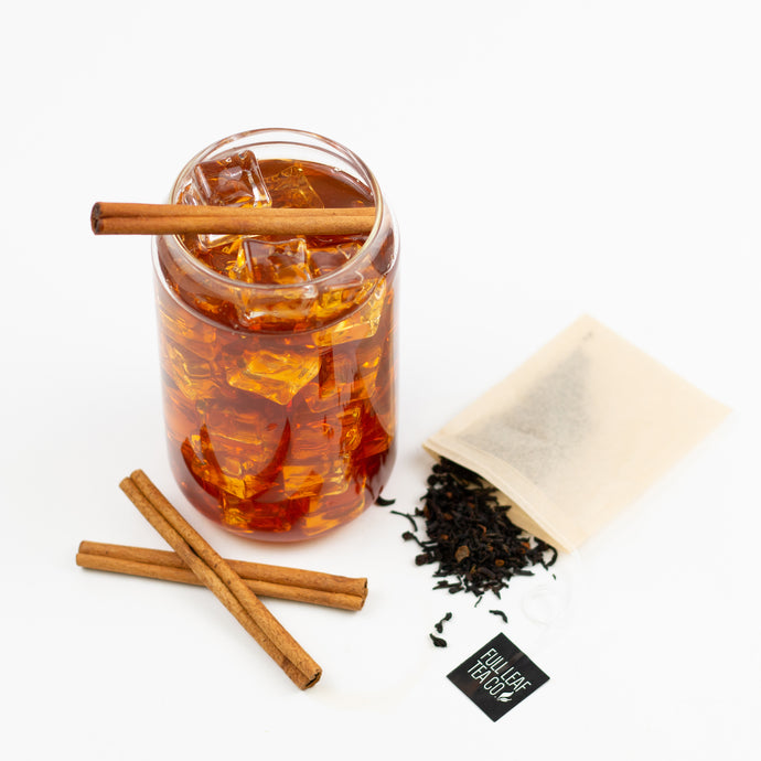 Glass of iced tea with cinnamon sticks, a bag of loose leaf tea, and a label on a white background