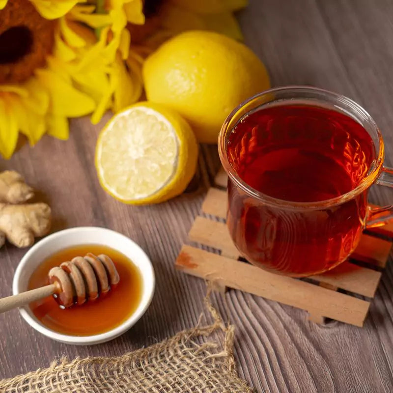 Immunity blend tea in glass next to bowl of honey and lemons behind