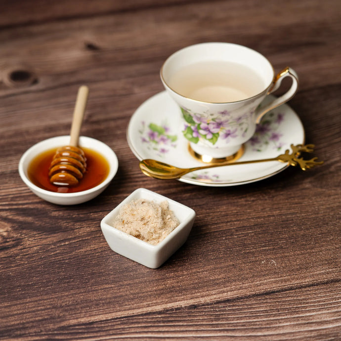 Teacup with floral design on a wooden table, accompanied by honey and sugar.