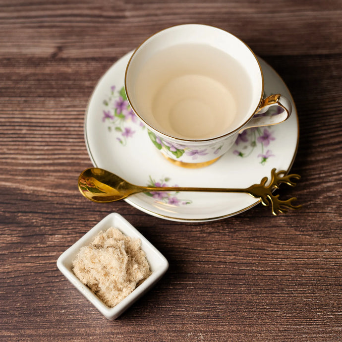 Teacup with saucer, spoon, and slippery elm in a bowl on a wooden surface