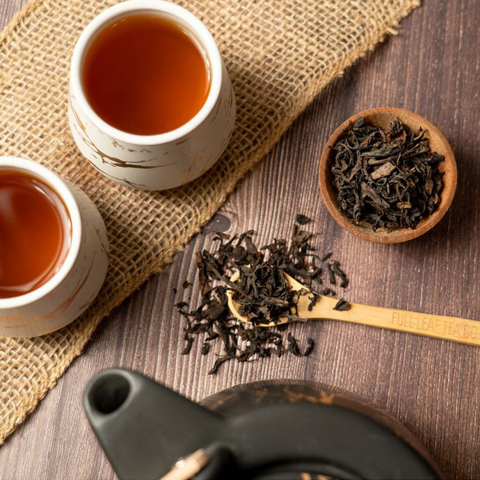 Two cups of tea with dry tea leaves and a teapot on a wooden surface.