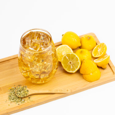 Glass of iced yerba mate tea on a wooden tray with sliced lemons, whole lemons, and a bamboo spoon labeled 'Full Leaf Tea Co' holding loose yerba mate leaves.